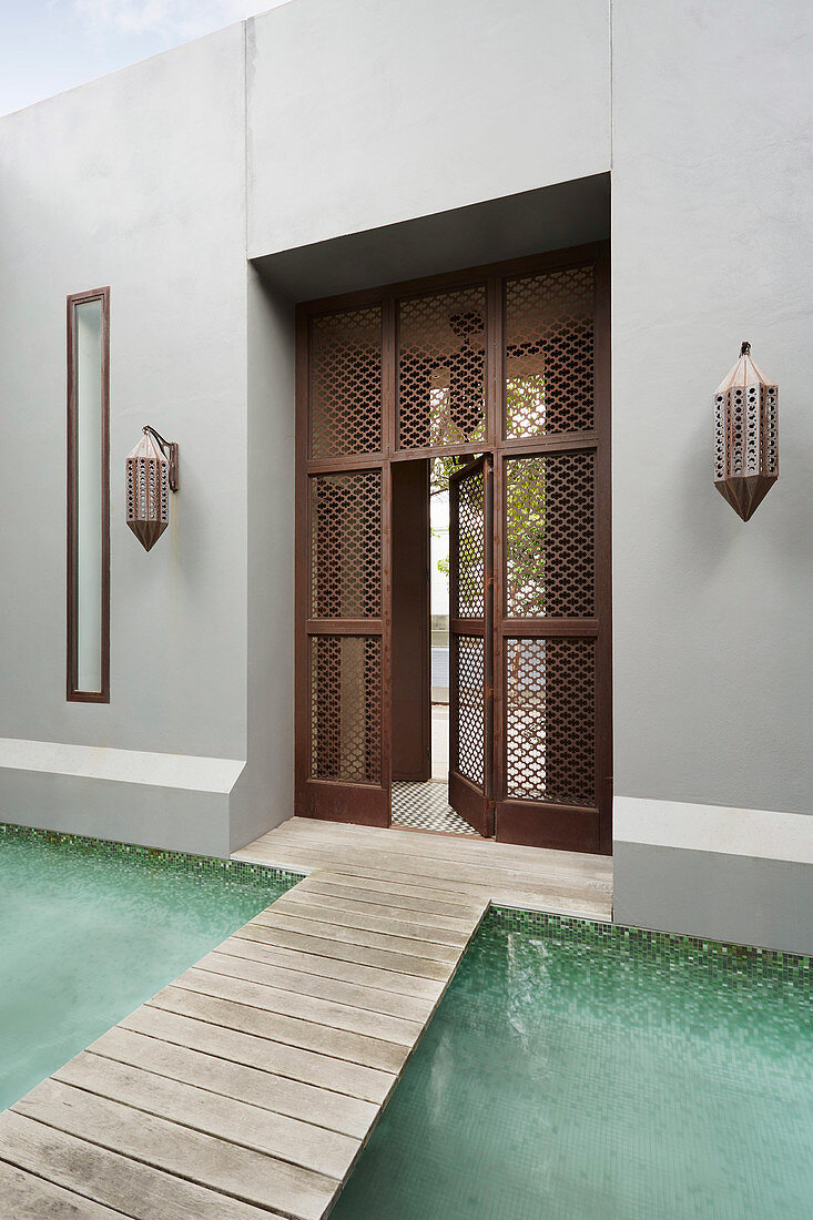 Steg über den Pool zum Haus mit Gittertür im marokkanischen Stil