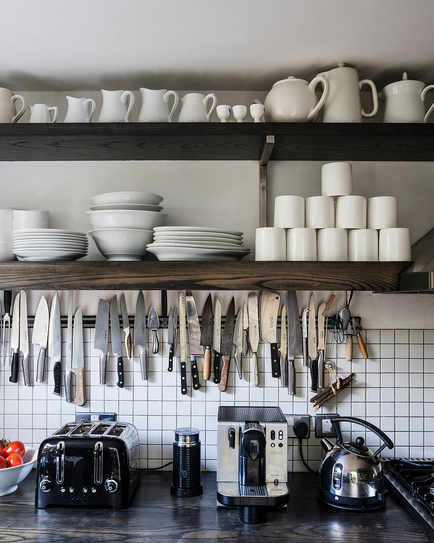 White crockery on open shelving above kitchen work top with knife rack, toaster and kettle