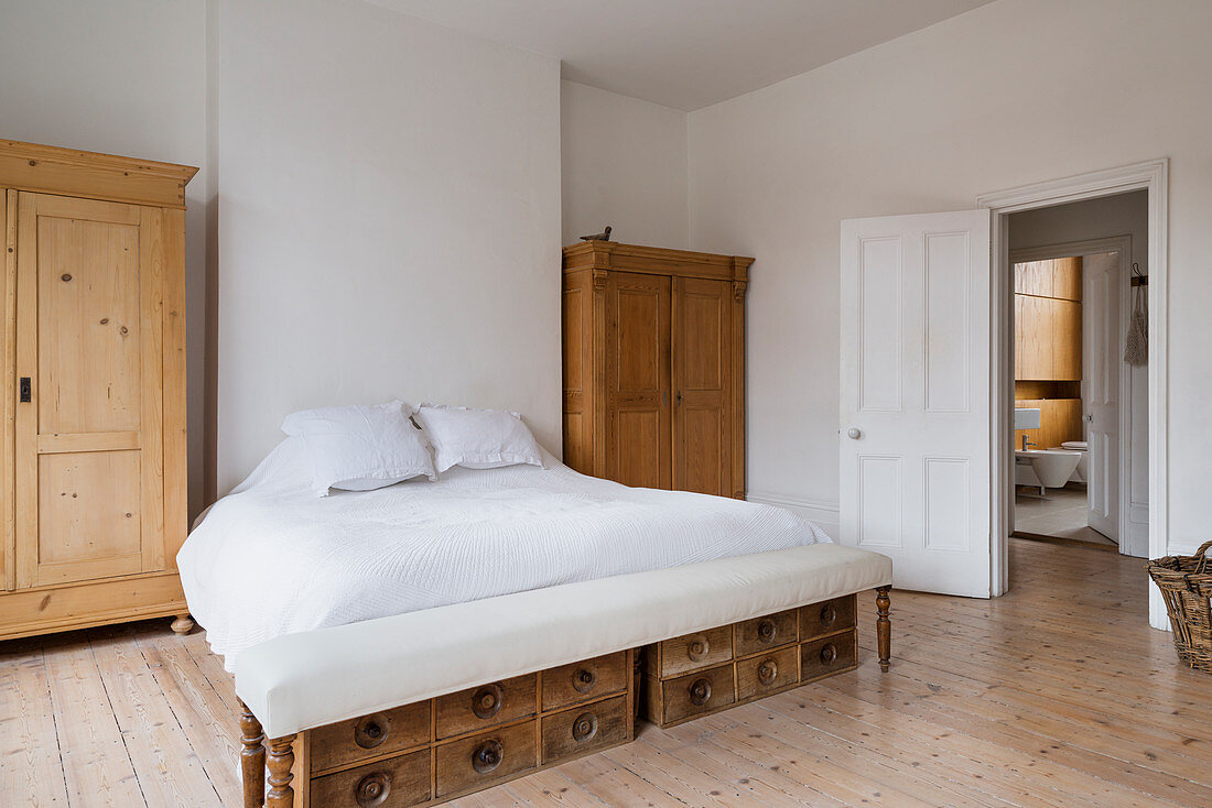 Large white bed in minimal white bedroom with wooden wardrobes and flooring
