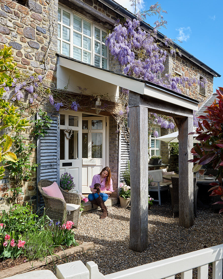 Wisteria growing on facade of stone house with woman and dog in entrance