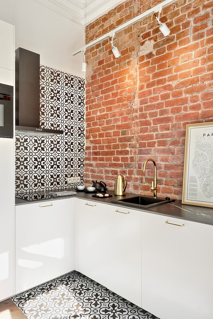 Kitchen with brick wall and black-and-white tiles on wall and floor in small apartment