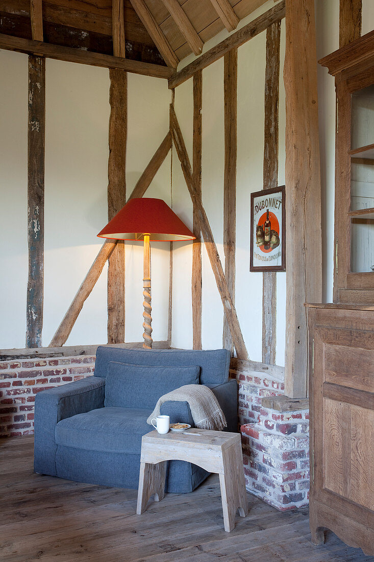 Stool, grey armchair and standard lamp in seating area in timber-framed house