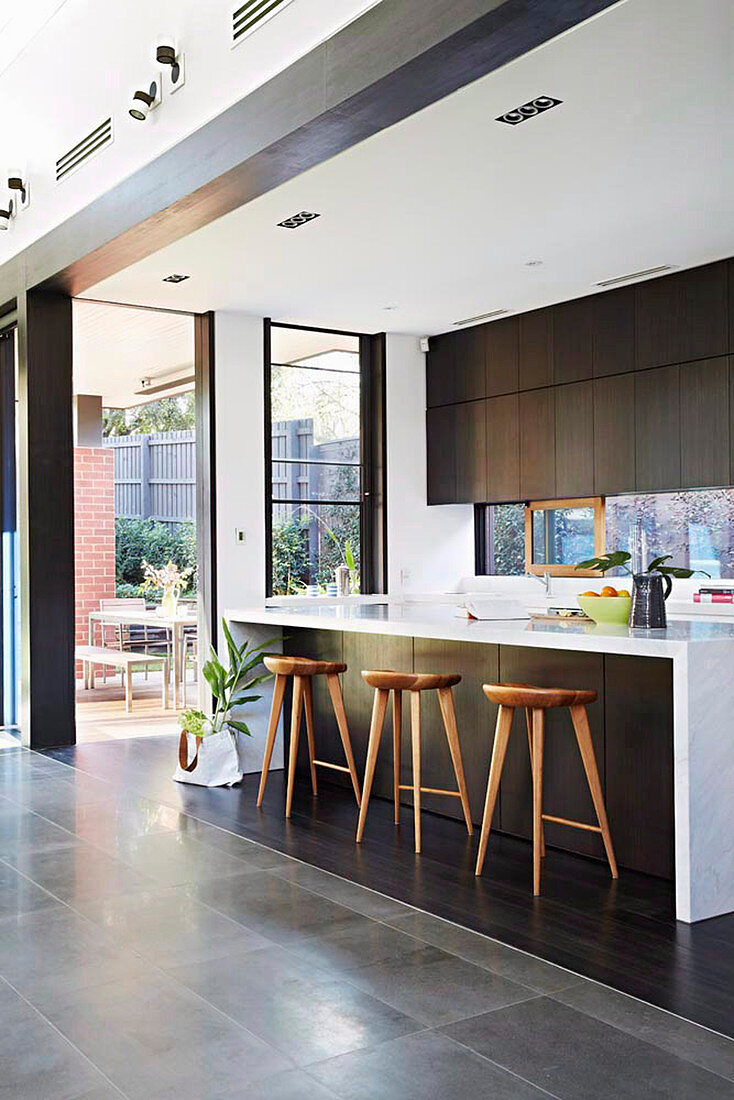 Kücheninsel mit Barhockern vor Terrassentür in eleganter Küche in offenem Raum