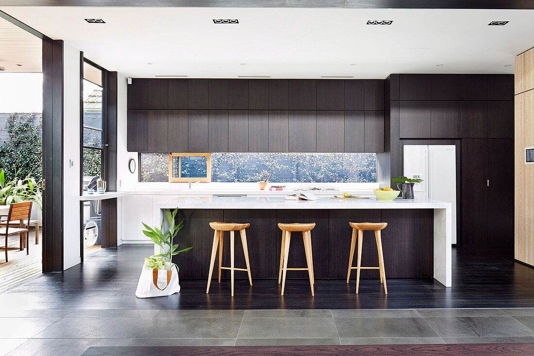 Kücheninsel mit Barhockern vor Terrassentür in eleganter Küche in offenem Raum