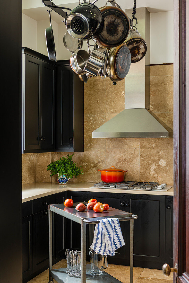 Compact kitchen with matt black lacquer cupboards and Corian worktops, cooking pots hang from the ceiling above a kitchen trolly