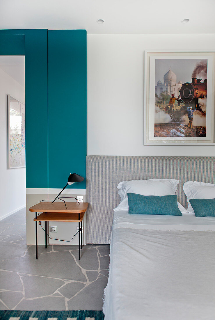 Doppelbett mit grauem Betthaupt und Beistelltisch im Schlafzimmer mit türkisfarbener Wandverkleidung
