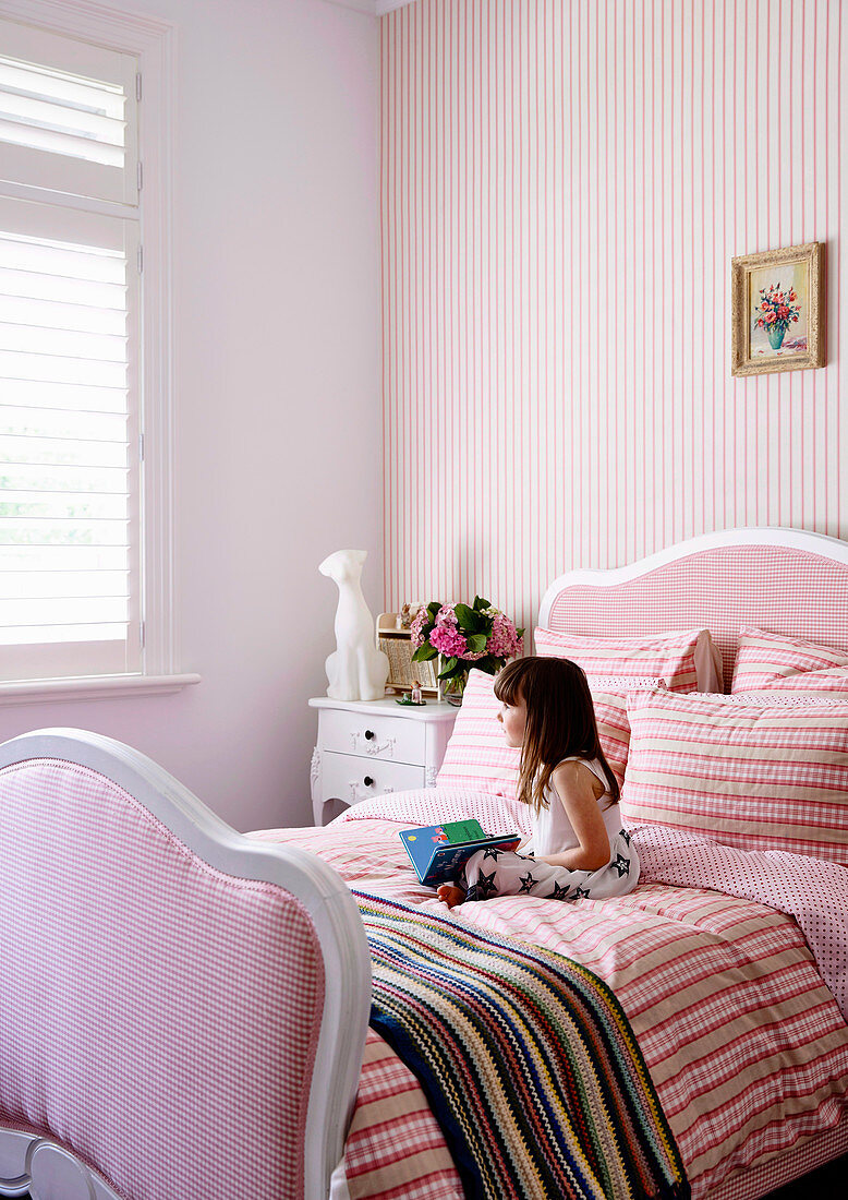 Mächen sitzt auf Bett mit rosa Bettwäsche im Mädchenzimmer