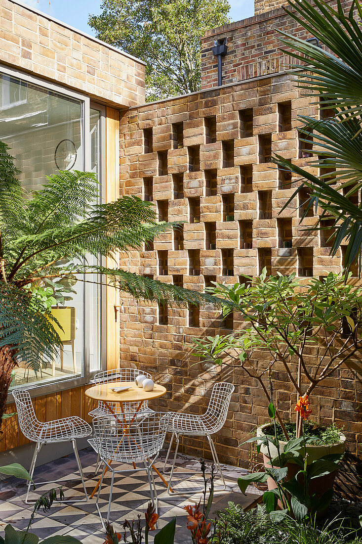 Outdoor furniture on tiled terrace against perforated brick wall