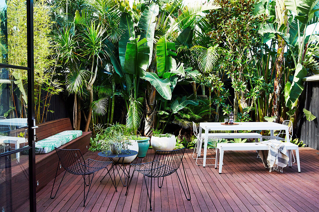 Holzterrasse mit Outdoormöbeln, umgeben von tropischen Pflanzen