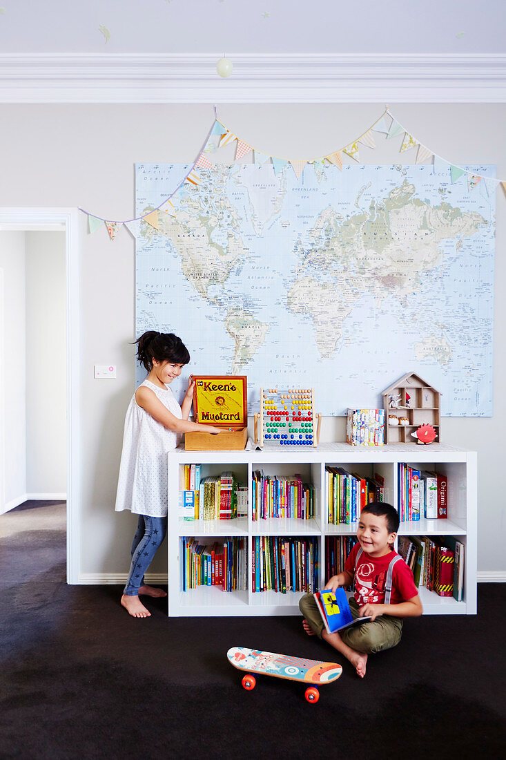 Mädchen und Junge im Kinderzimmer mit Bücherregal und Landkarte an der Wand
