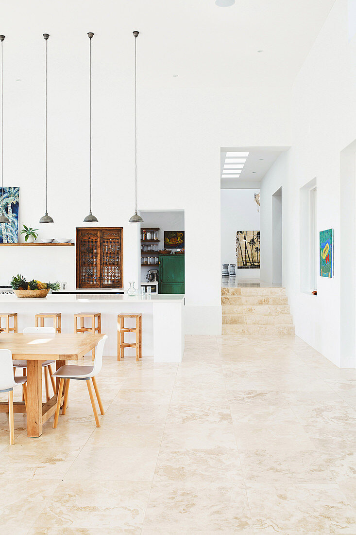 Essbereich vor Küchentheke mit Pendelleuchten in offenem Wohnraum, im Hintergrund Durchgang mit Treppe