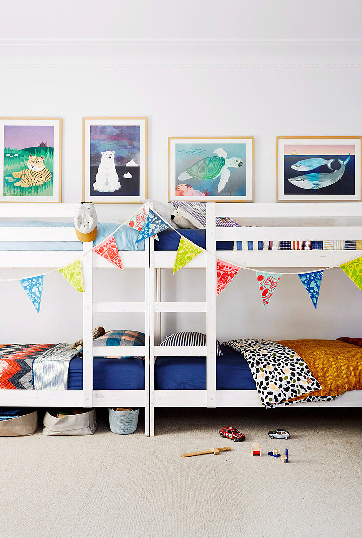 Zwei Etagenbetten mit Wimpelkette dekoriert, darüber Bilder an der Wand im Kinderzimmer