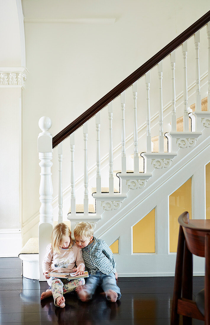 Elegantes Treppenhaus mit weißer Treppe und dunklem Dielenboden, lesende Kinder auf dem Boden