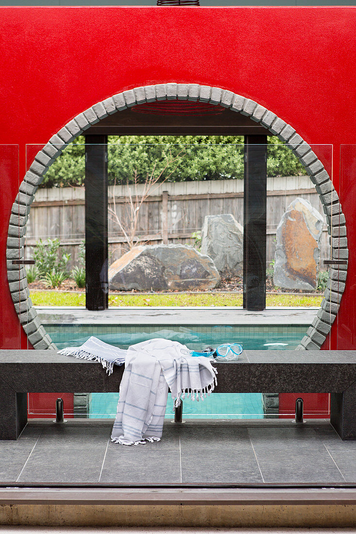 Stone bench with bath towel and diving goggles in front of a round neckline, with a view of the swimming pool