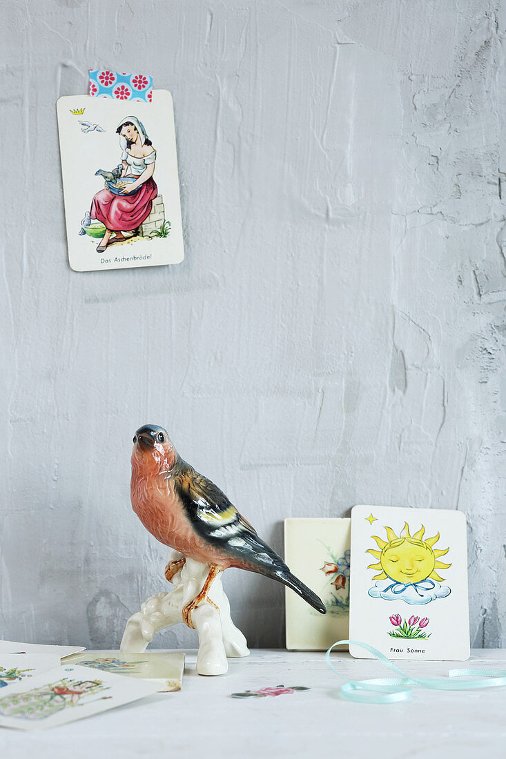Porzellanvogel und nostalgische Spielkarten vor grauer Wand