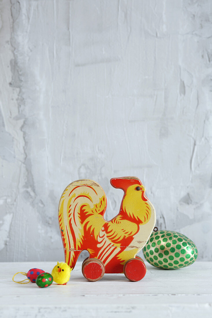 Old toy cockerel and Easter decorations against grey wall