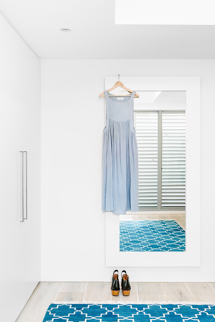 Sommerkleid an Wandspiegel, blauer Teppich und Kleiderschrank in weißem Schlafzimmer