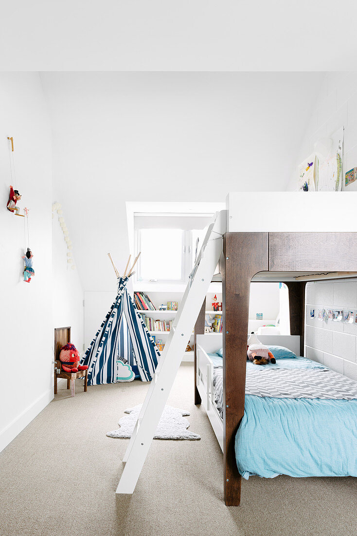 Stockbett mit Bettleiter in weißem Kinderzimmer, im Hintergrund Tipi