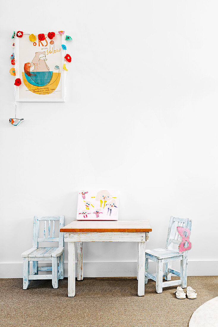 Kindertisch mit zwei Stühlen vor weißer Wand, darüber Bild mit Girlande