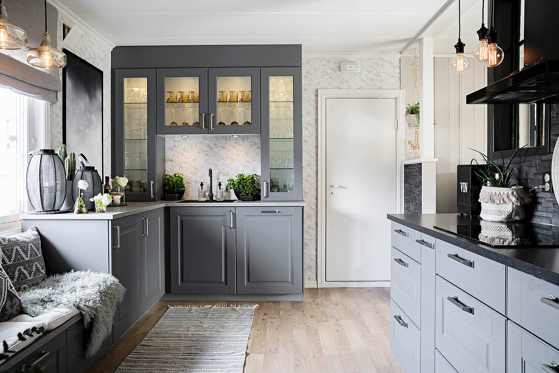 Open-plan country-house kitchen with grey cupboards and illuminated glass-fronted dresser