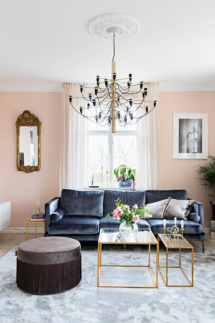 Dark velvet sofa, delicate coffee table and pouffe in pale pink living room