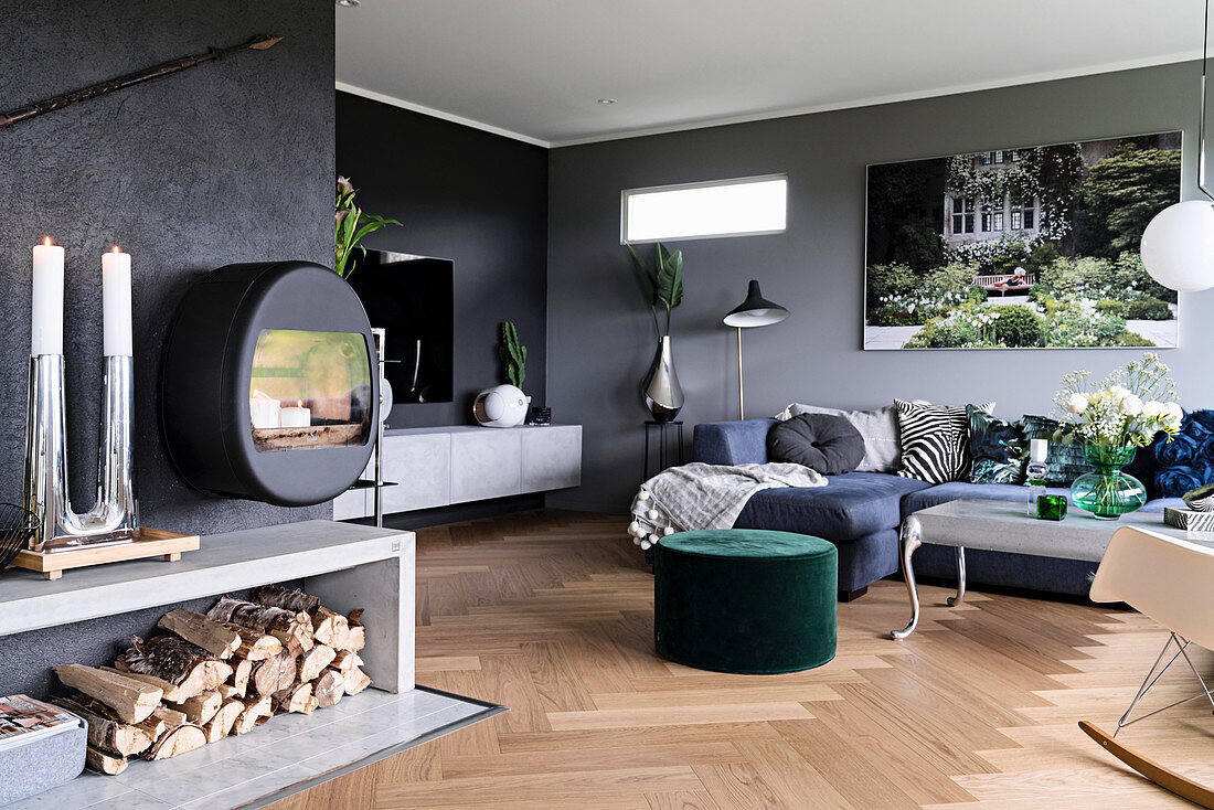 Large living room with grey walls, fireplace and firewood store, blue sofa combination and green pouffe