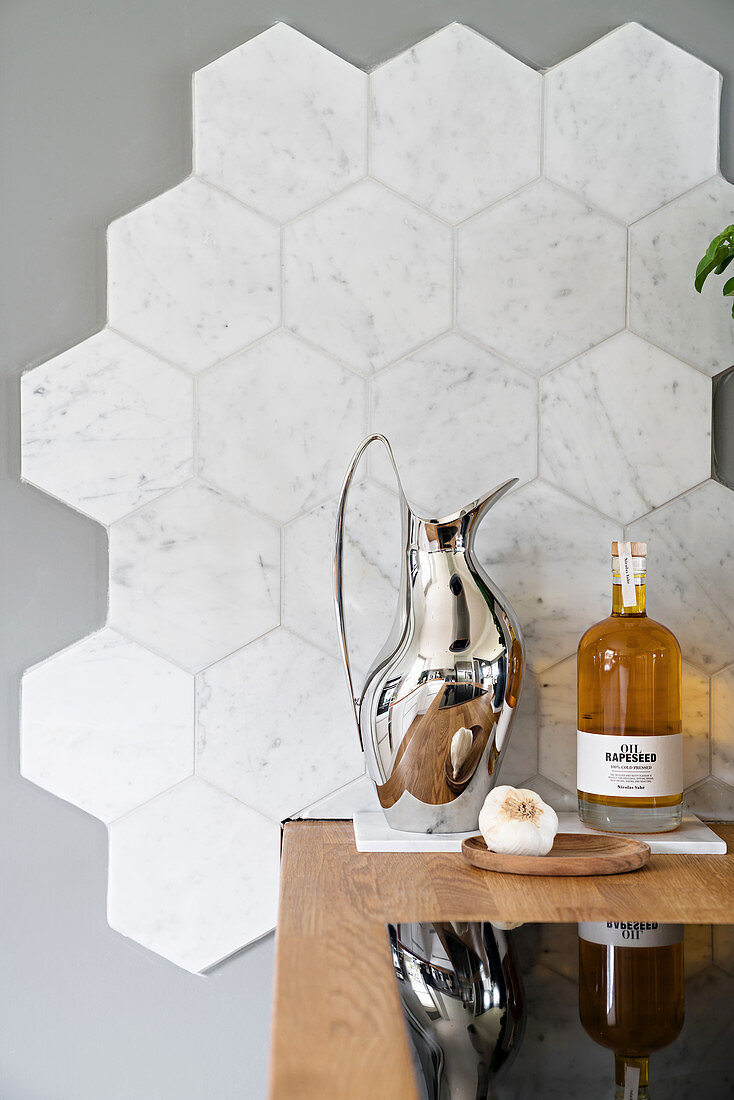 Edelstahlkanne und Ölflasche auf Kochtheke mit Holzarbeitsplatte, Marmorfliesen an grauer Wand