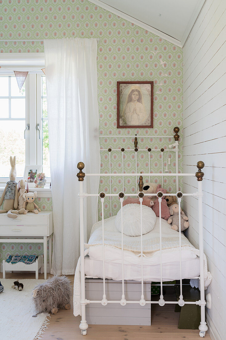 Soft toys on white metal bed and green wallpaper in child's bedroom