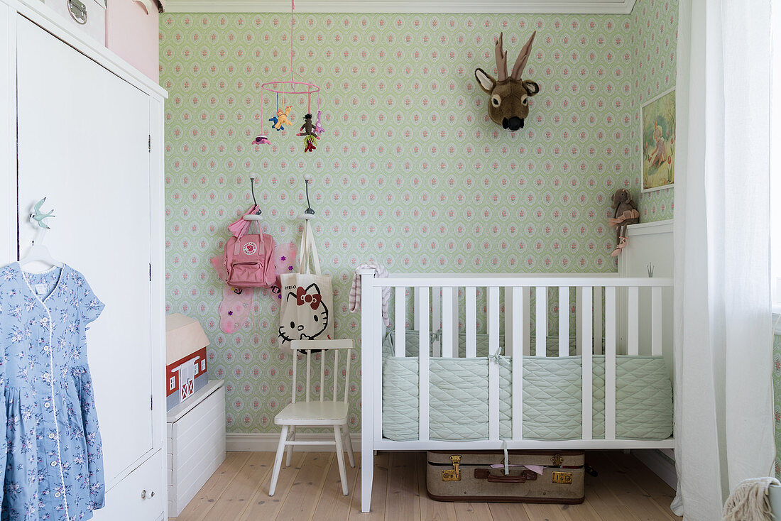 Weißes Gitterbett und Schrank im Kinderzimmer mit grüner Tapete