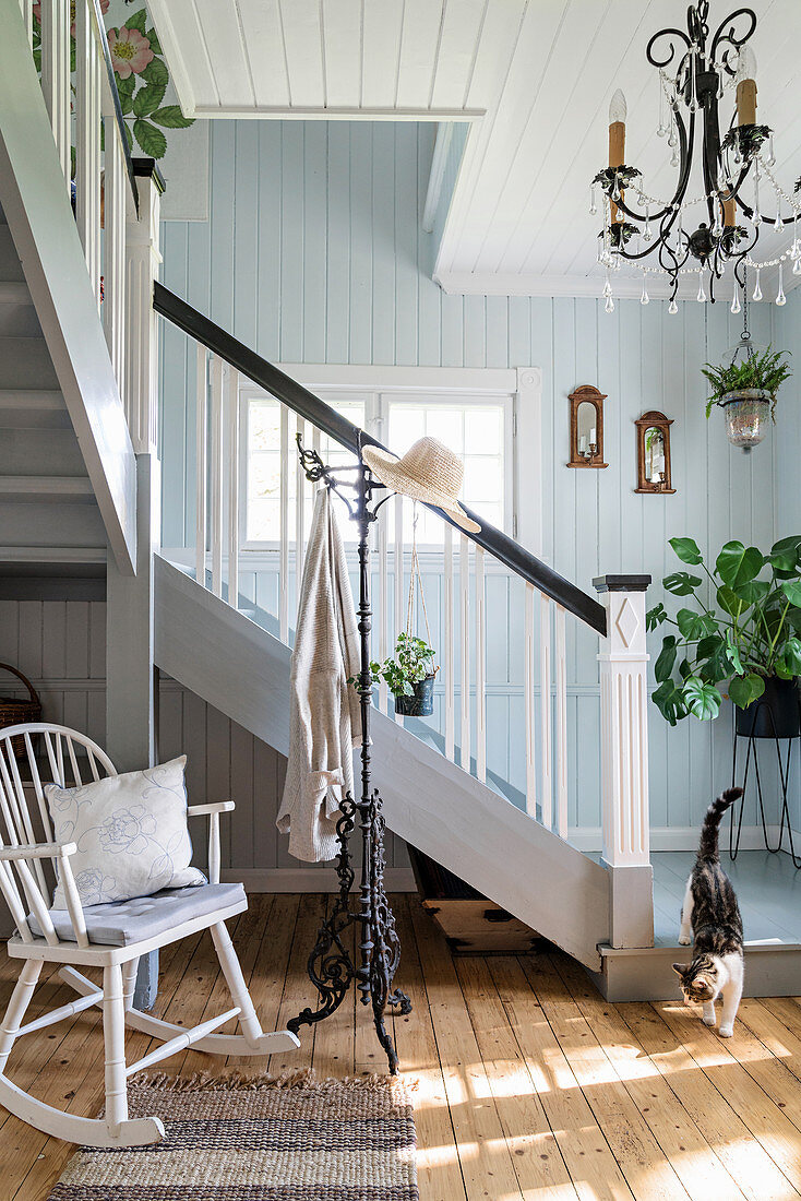 Schaukelstuhl vor Treppe in Eingangshalle mit Holzdielenboden und hellblauer Wand