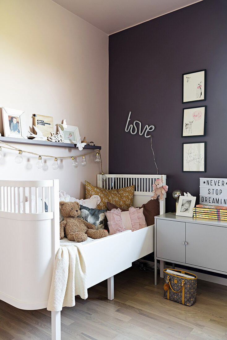 Weißes Kinderbett und Nachtschränkchen im Mädchenzimmer mit rosa und lila Wänden