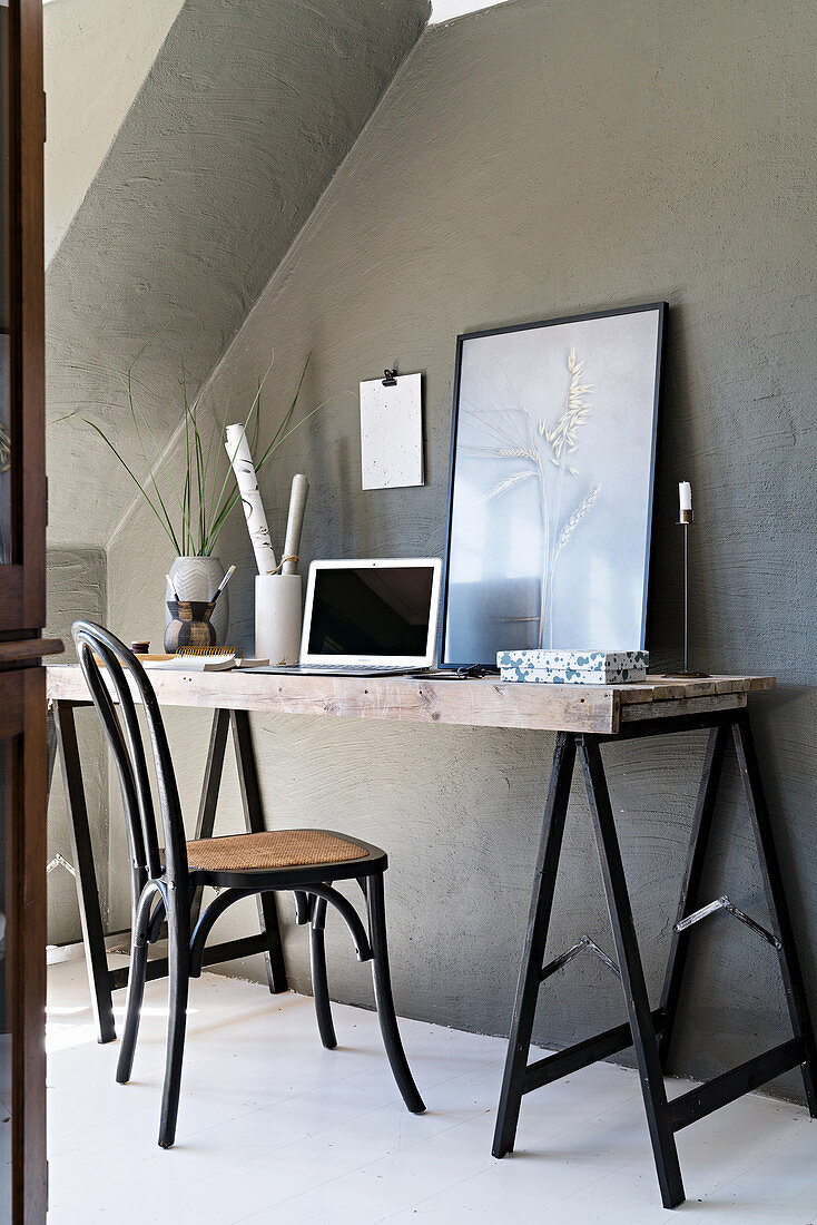 Desk made from trestles against grey wall below sloping ceiling