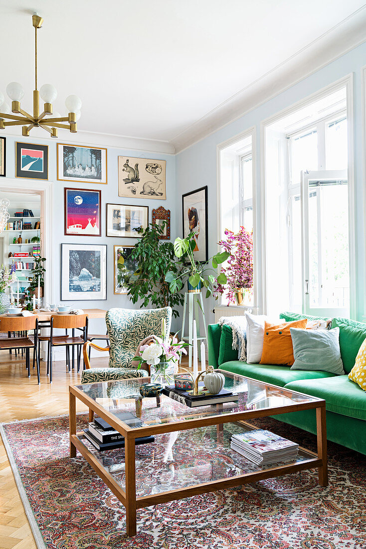 Green sofa and glass coffee table in period apartment with dining table in background next to gallery of pictures