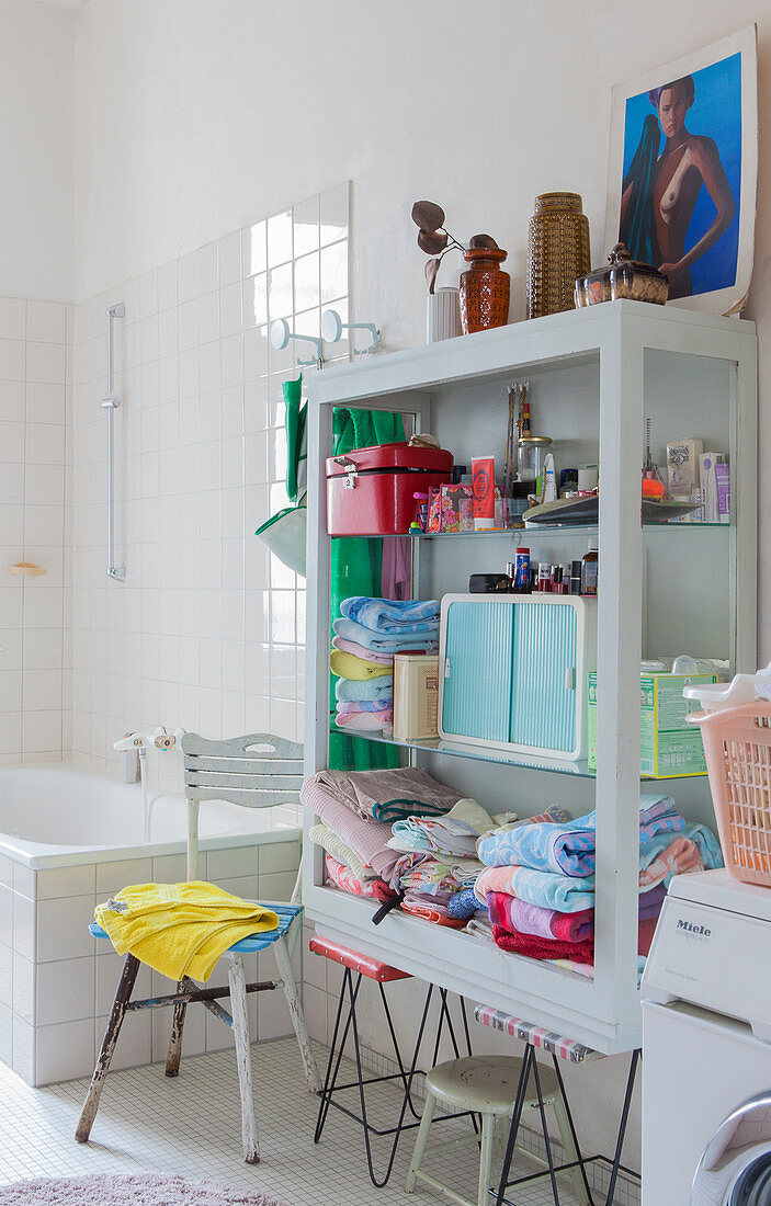 Open-fronted cupboard on two retro stools used as shelves in bathroom