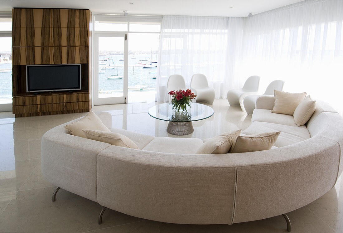 White designer sofa in front of window and wood-clad TV cabinet in open-plan interior