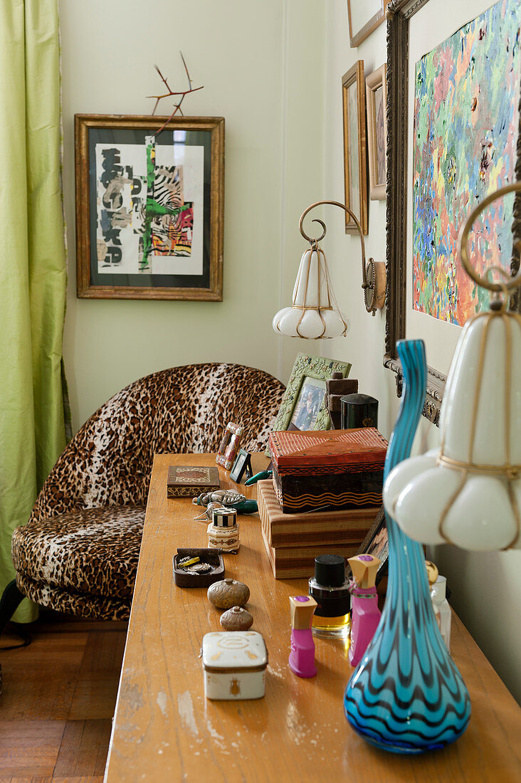 Verschiedene Kästchen und Vase auf Sideboard neben Sessel mit Leopardenmuster im Schlafzimmer