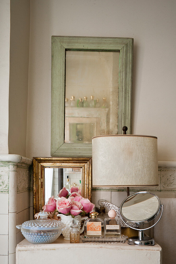 A selection of mirrors and perfumes on cabinet in shabby chic tiled bathroom