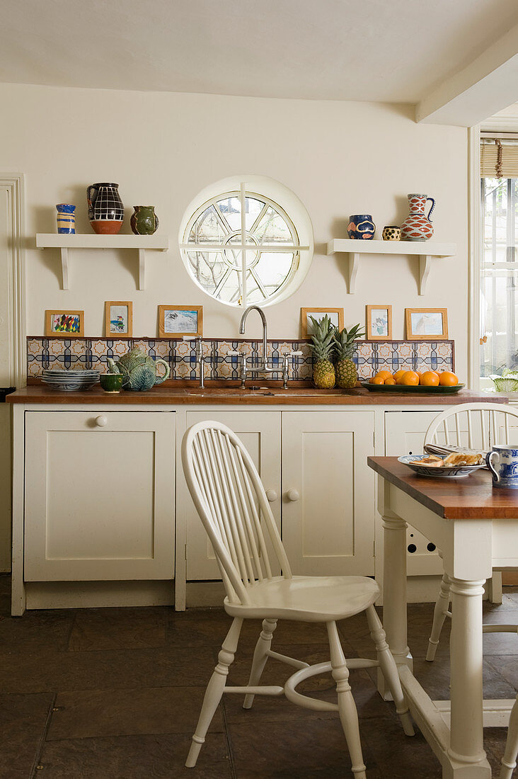 Ländlich rustikale Küche mit weißen Küchenmöbeln und Rundfenster über Küchenzeile