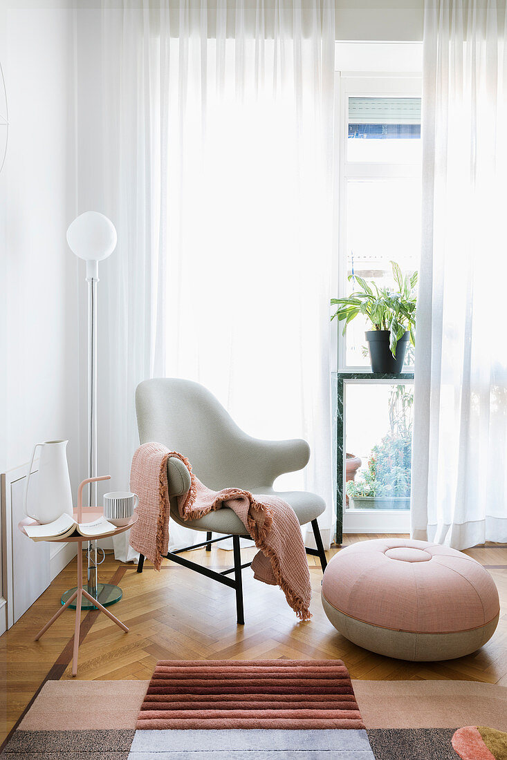 Armchair with round pouffe and pink accessories next to window