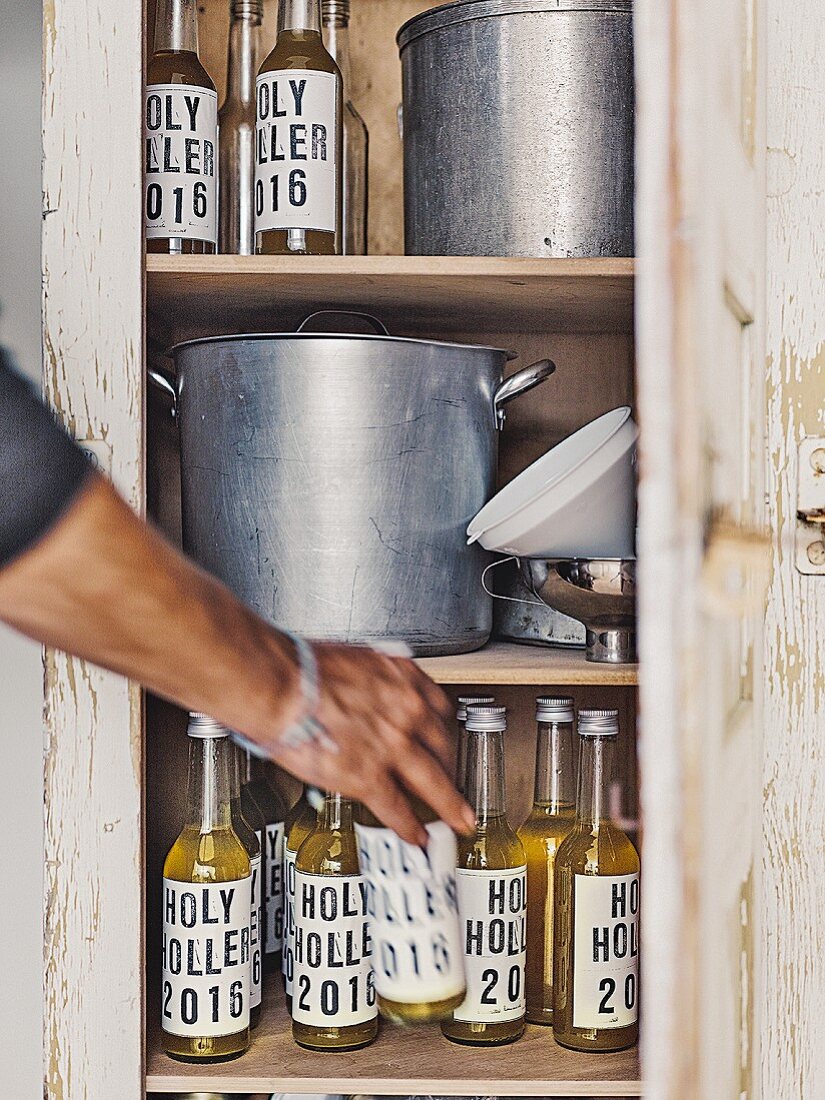 Homemade elder lemonade in labelled bottles in a vintage kitchen cupboard