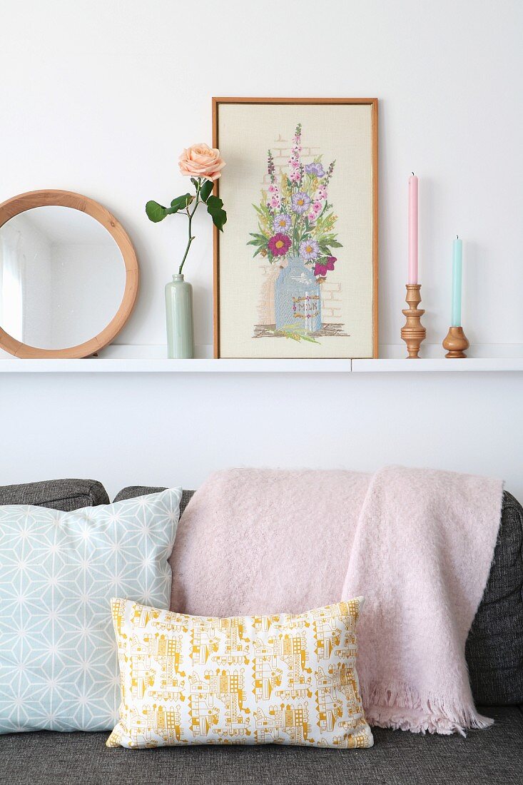 Bilderleiste mit Accessoires über Sofa mit pastellfarbenen Kissen