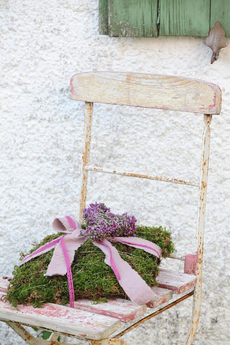Romantic cushion of moss on vintage wooden chair against house façade