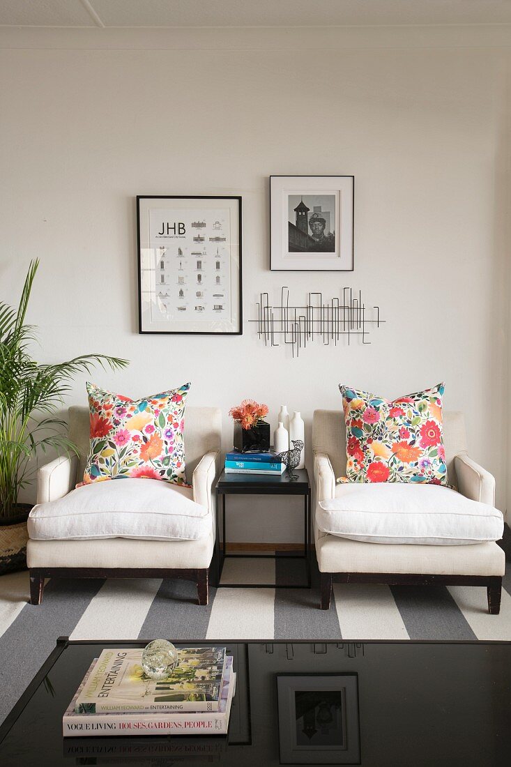 Two white armchairs with colourful floral scatter cushions against wall