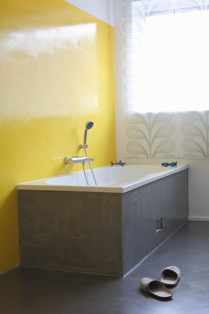 Grey-clad bathtub against bright yellow wall