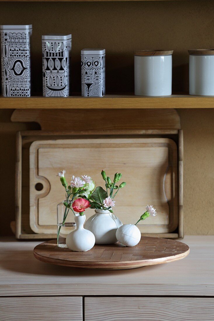 Small vases of flowers on lazy Susan covered in patterned wood veneer in kitchen