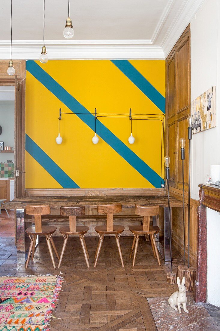 Wand mit diagonalen Streifen über dem Esstisch mit Holzstühlen