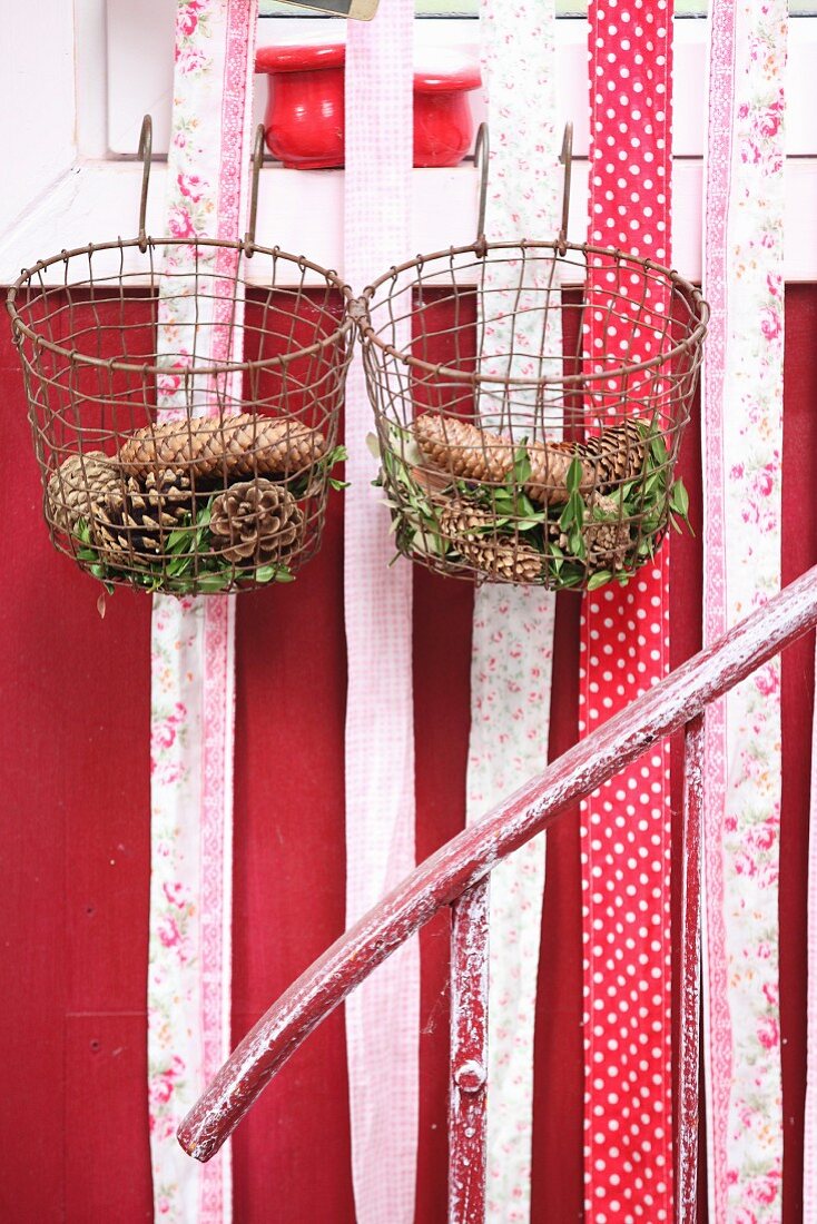 Various pine cones and box sprigs in vintage wire baskets and strips of fabric hung from window frame