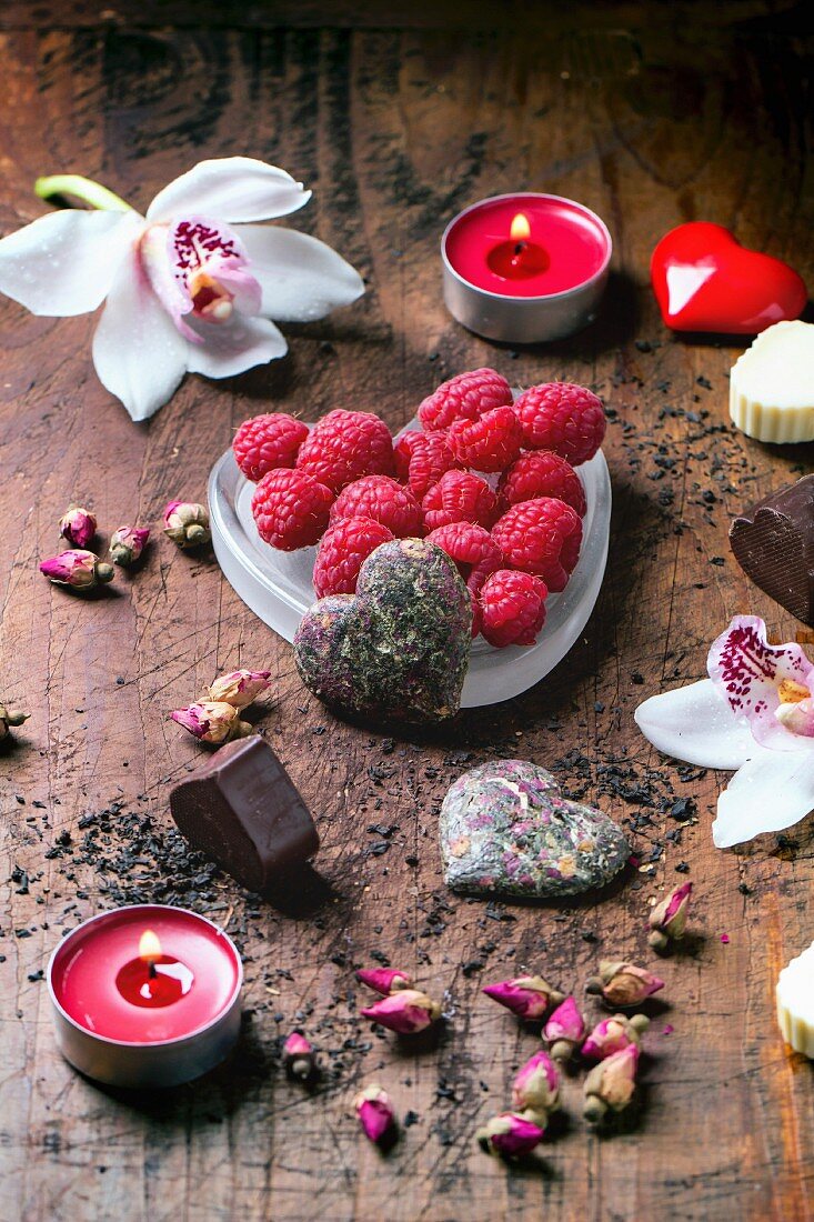 Chocolate candies heart shaped with dry tea roses, fresh raspberries and orchids for Valentine s Day