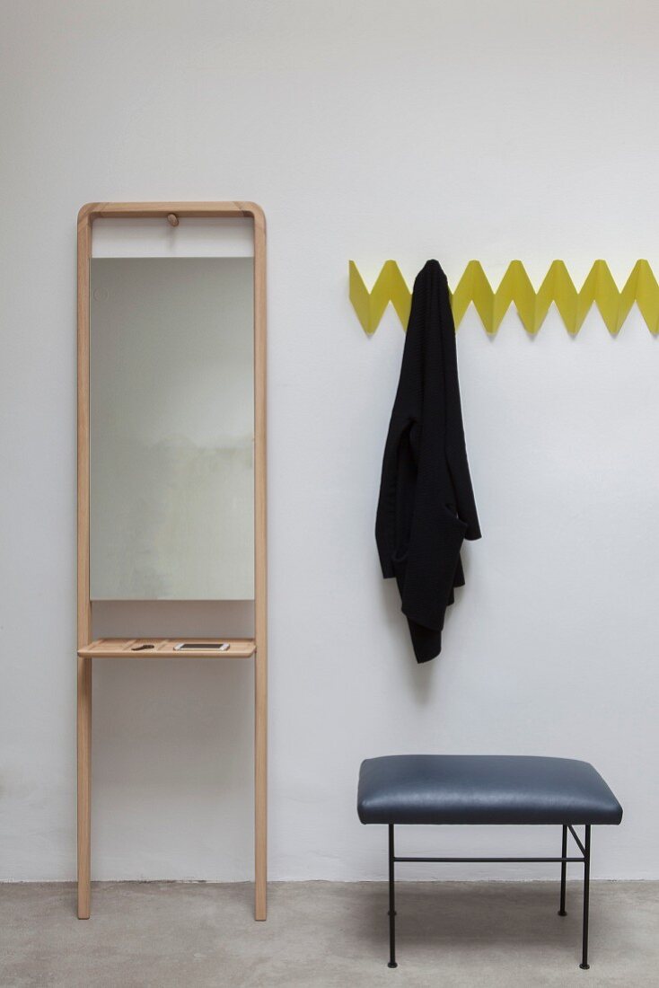 Yellow, zigzag, wall-mounted coat rack next to stool and simple mirror on stand with shelf