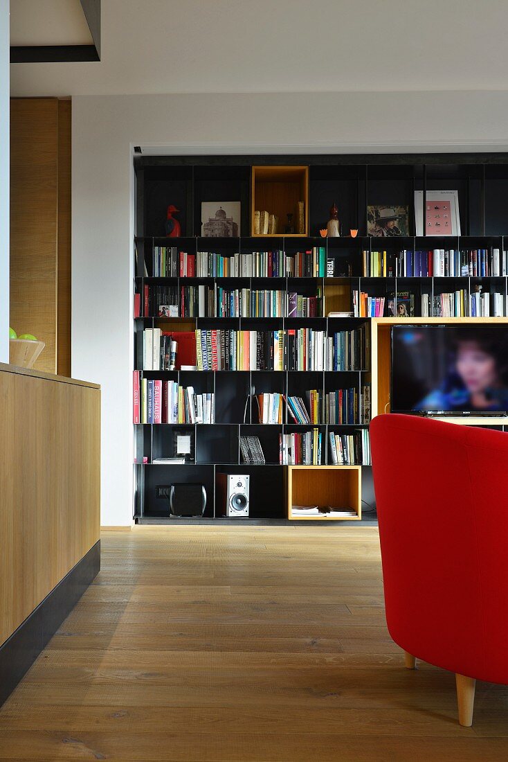 Schwarzes Metall-Bücherregal mit integiertem Fernseher in offenem Wohnbereich mit Eichenparkett